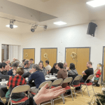 Dr Popkins standing beside a Christmas tree at the London Basque Society festive meal, community hall in background
