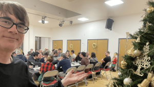 Dr Popkins standing beside a Christmas tree at the London Basque Society festive meal, community hall in background