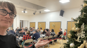 Dr Popkins standing beside a Christmas tree at the London Basque Society festive meal, community hall in background